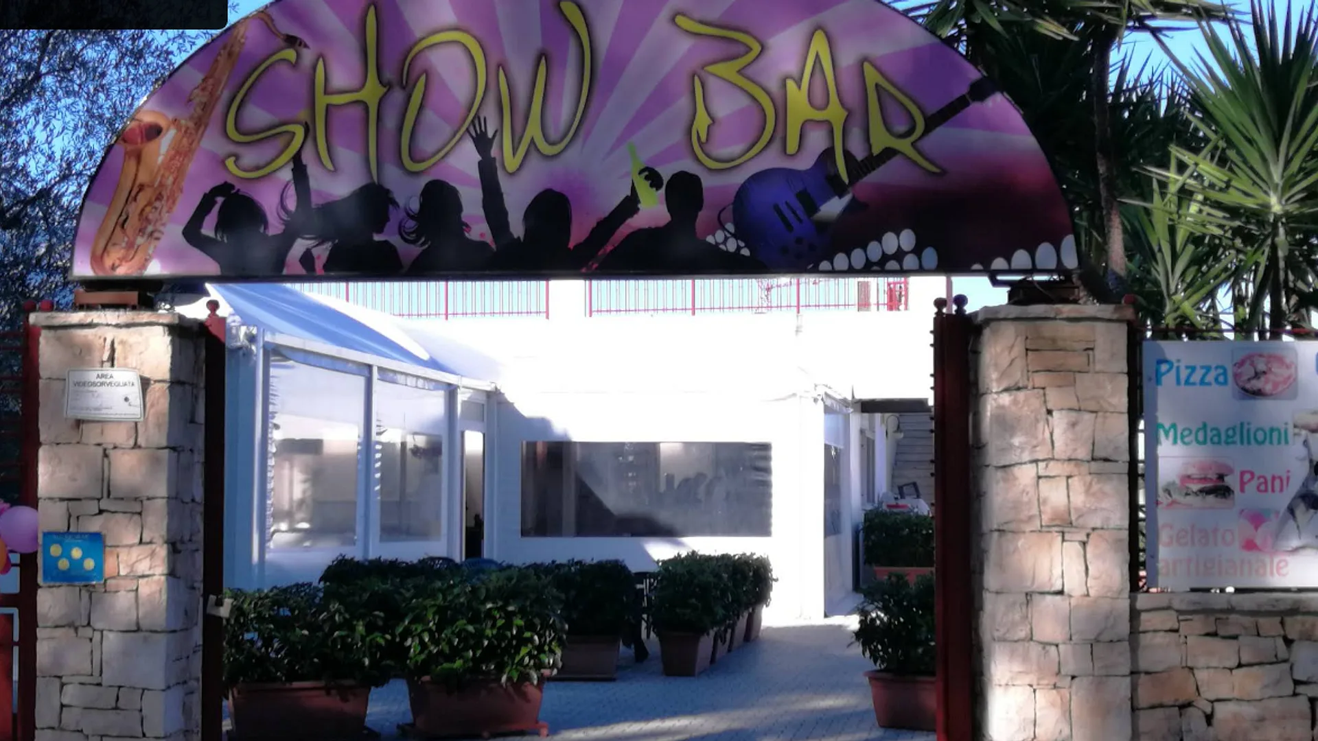 L'ingresso di Show Lounge: l'insegna ad arco sui pilastri in pietra, tra le piante